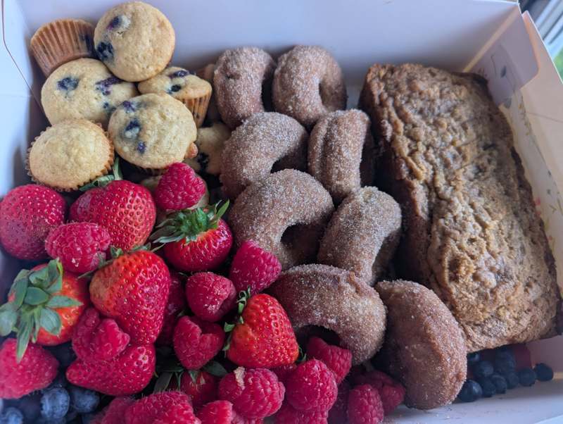 Brunch box filled with mini blueberry muffins, cinnamon-sugar donuts, coffee cake, and fresh berries